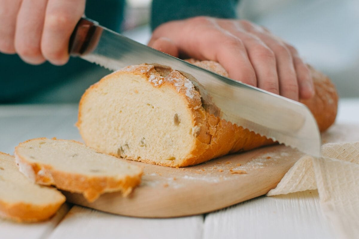 Bàn tay nam giới cắt bánh mì lúa mì trên thớt gỗ, chuẩn bị cho mẹo làm mềm bánh mì cứng tại nhà