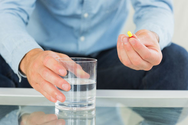 Ảnh một người đàn ông cầm viên thuốc màu vàng đỏ và một cốc nước
