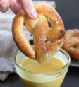 Bàn tay cầm bánh pretzel mềm màu nâu nhạt với muối trắng và phủ sốt mù tạt mật ong vàng
