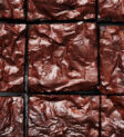 Hình ảnh một khay bánh brownies sô cô la đã nướng, được cắt miếng và nhìn từ trên xuống, thể hiện lớp vỏ mỏng bóng bẩy.