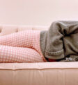cropped photo showing the legs and torso of a woman laying on her side on a couch holding her stomach due to abdominal pain