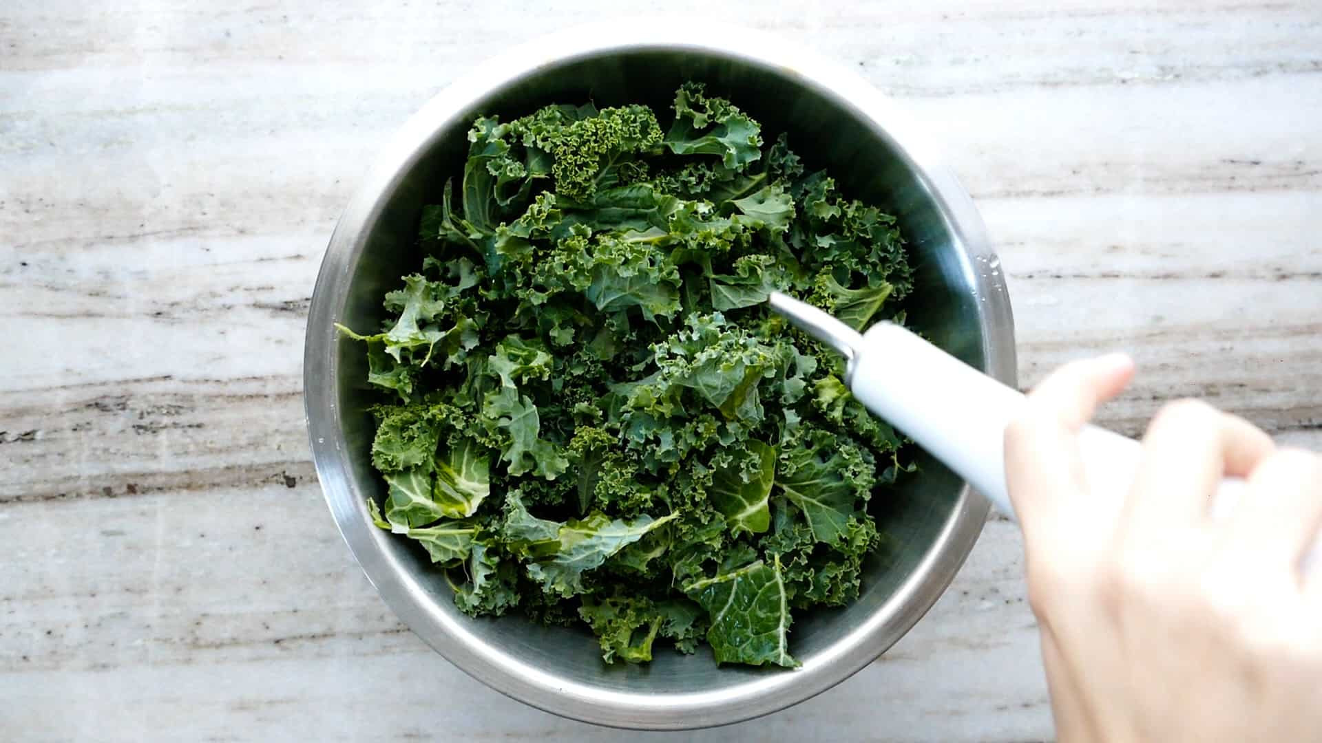 Người phụ nữ đang rưới dầu ô liu lên bát lá cải xoăn sống trên quầy