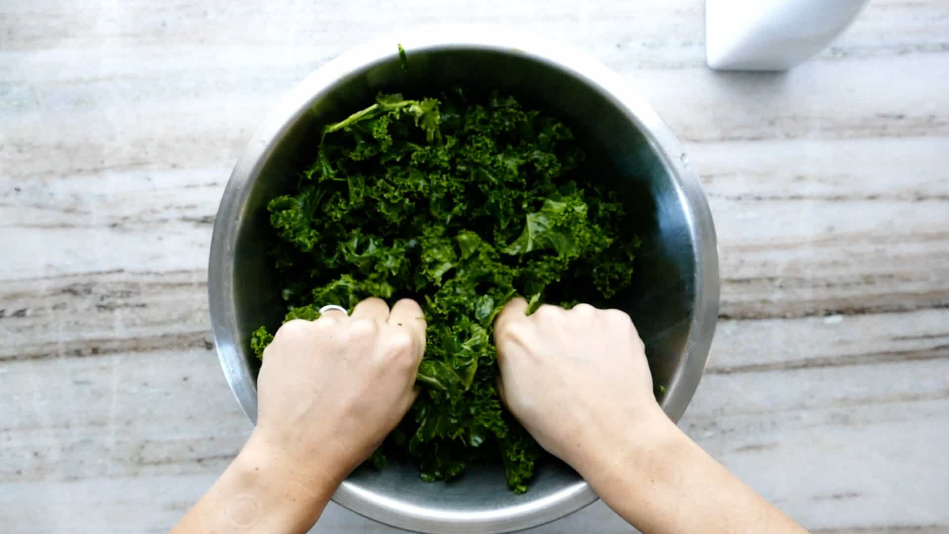 Người phụ nữ dùng tay xoa bóp lá cải xoăn sống với dầu trong bát trộn