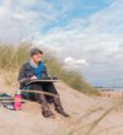 Nina Squire on the beach with sketchbook and flask