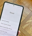 Điện thoại Samsung Galaxy trên tay người dùng với menu Reset hiển thị các tùy chọn: Reset all settings, Reset network settings, Reset accessibility settings, Factory data reset.