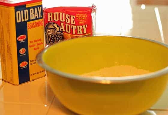 A green bowl with seafood breader in it. A bag of breader and seasoning in background.