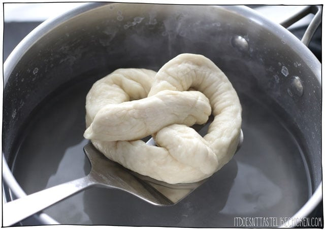 Một chiếc bánh pretzel mềm thuần chay hoàn hảo, được trình bày trên đĩa gỗ với một chén mù tạt vàng óng.