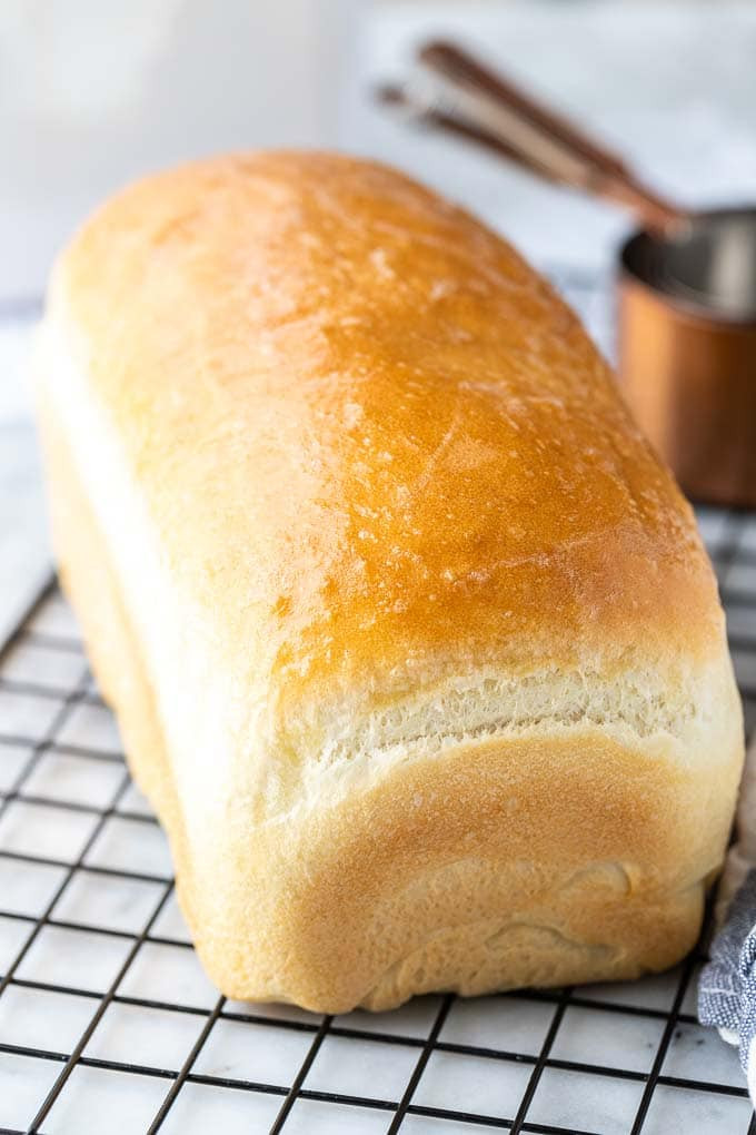 Một ổ bánh mì trắng trên giá làm mát màu đen bên cạnh một số cốc đo màu đồng